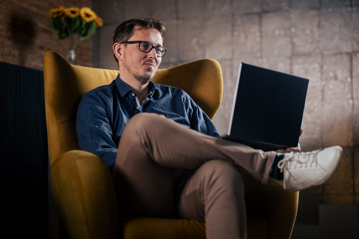 Frank van Delden, de maker van Grip op mijn Geld, zit in een gele fauteuil en werkt op zijn laptop.